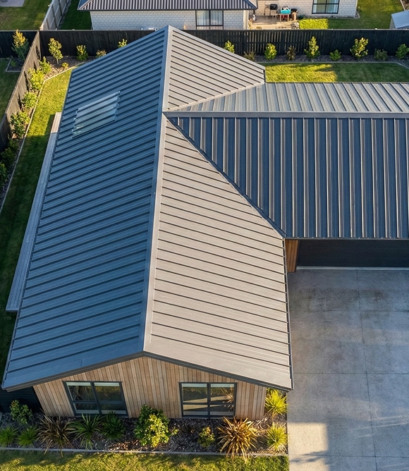 A high-angle drone shot showcasing the precision-cut valleys and ridges of a multi-gabled dark grey long-run metal roof on a new residential development.
